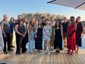A group of University of Pennsylvania students and professors stands on a rooftop in Athens with the Acropolis in the background.